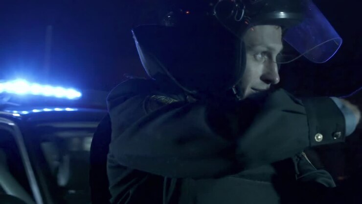 Police officer with a gun on the background of flickering flashers