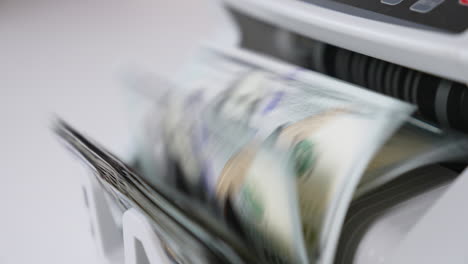 american banknotes rotating quickly in the slot of cash counting machine. close up. blurred background.