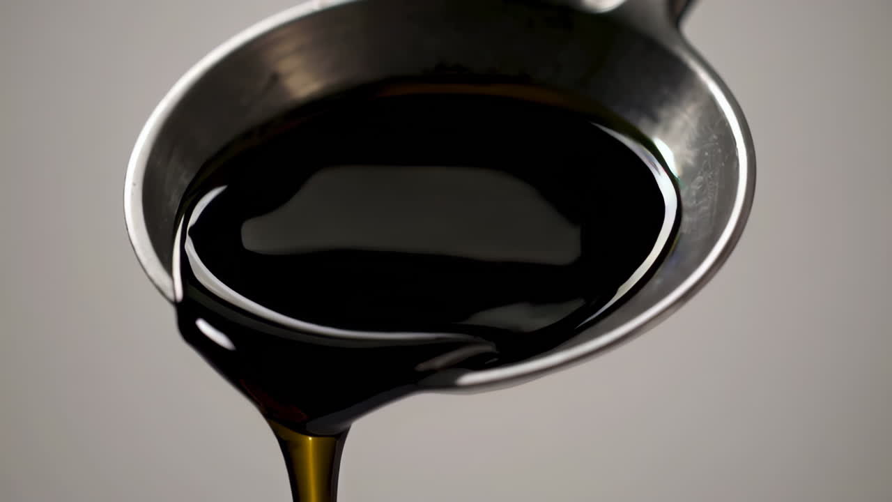 Dark Liquid Pouring from Metal Measuring Cup