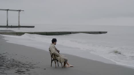 hombre solitario sentado a la orilla del mar en un día nublado y nublado justo antes de que el día se convierta en noche