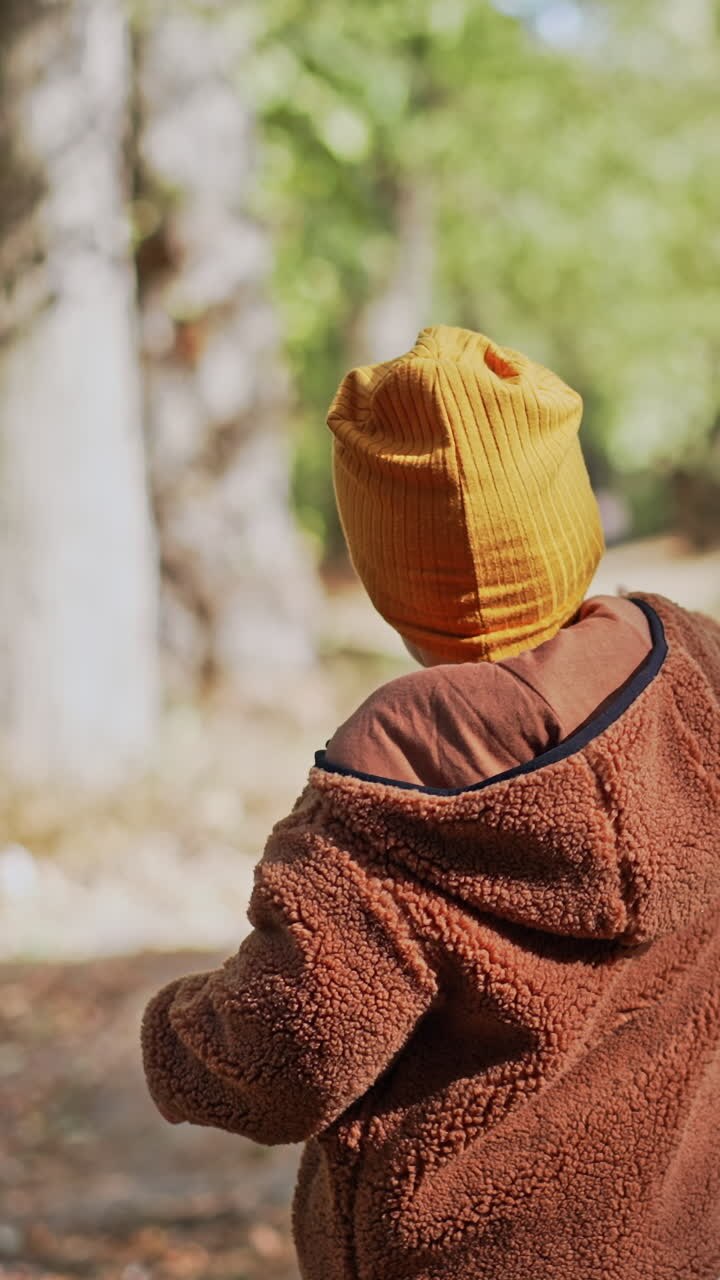 Un adorabile bambino che indossa un cappellino giallo, una tuta e una giacca calda cammina nel parco. Un neonato corre lungo il sentiero indicando verso l'alto con un dito.