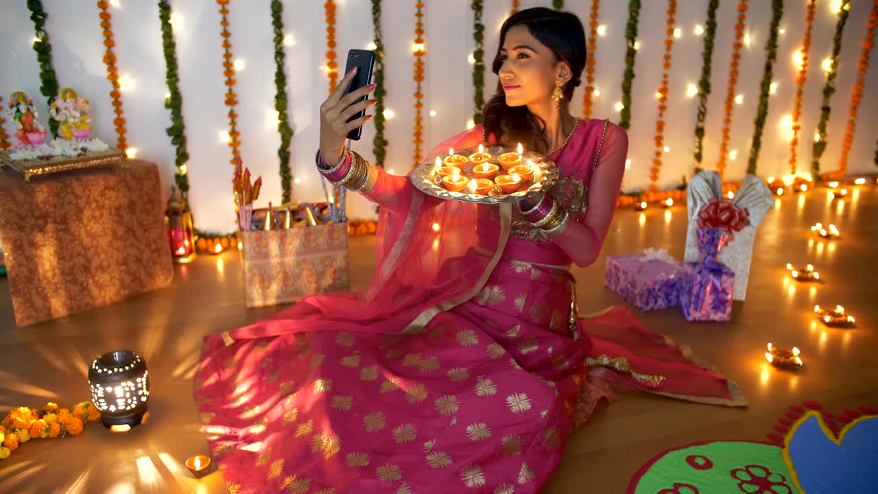 Pretty Indian lady enjoying while taking selfies with burning Diyas on Diwali festival