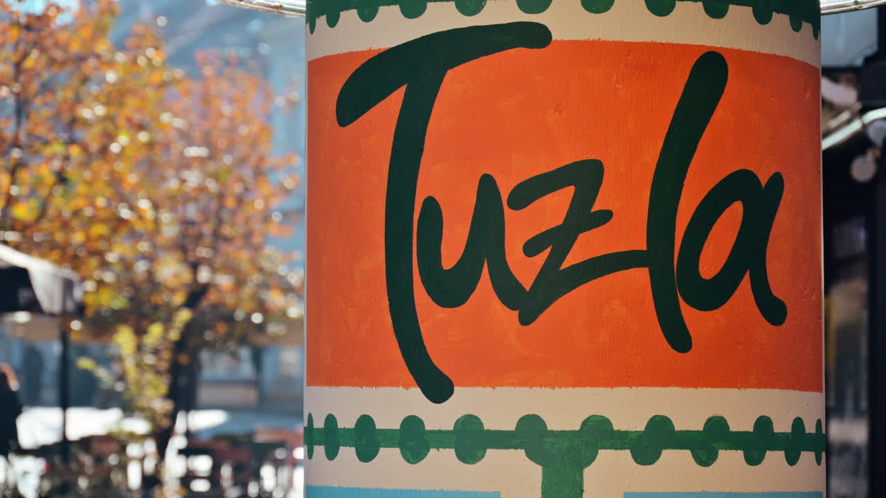 Nome Tuzla pintado em um poste de rua na Bósnia e Herzegovina, com uma rua da cidade desfocada ao fundo