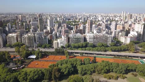 Buenos-Aires-aerial-view-of-tennis-courts-city-park-beside-highway-and-skyscrapers,-Bosques-de-Palermo-Tres-de-Febrero-Park,-drone-shot