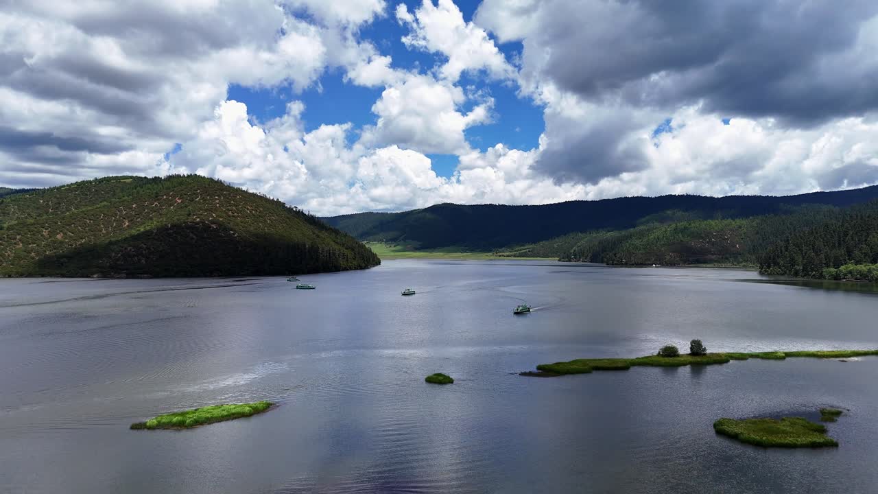 Potatso National Park Shangri-la Yunnan China, aerial dolly above alpine lake with small boats, grassy islets, and forested mountains under dramatic clouds