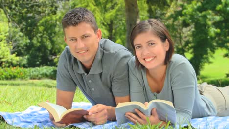 una pareja de jóvenes sonrientes leyendo al aire libre.