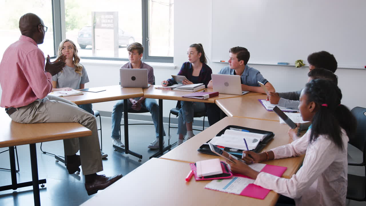 tutor de secundaria sentado en el escritorio y enseñando clase disparado en cámara lenta