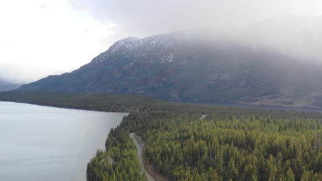 Imágenes-De-4k-De-Drones-Volando-Sobre-Una-Carretera-Remota-Al-Lado-Del-Lago-En-Las-Montañas