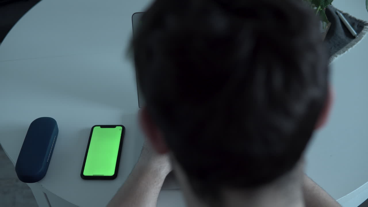 탑 뷰, 남자가 휴대폰을 터치하여 무언가를 변경하고, 휴대폰 화면은 그린 스크린이에요