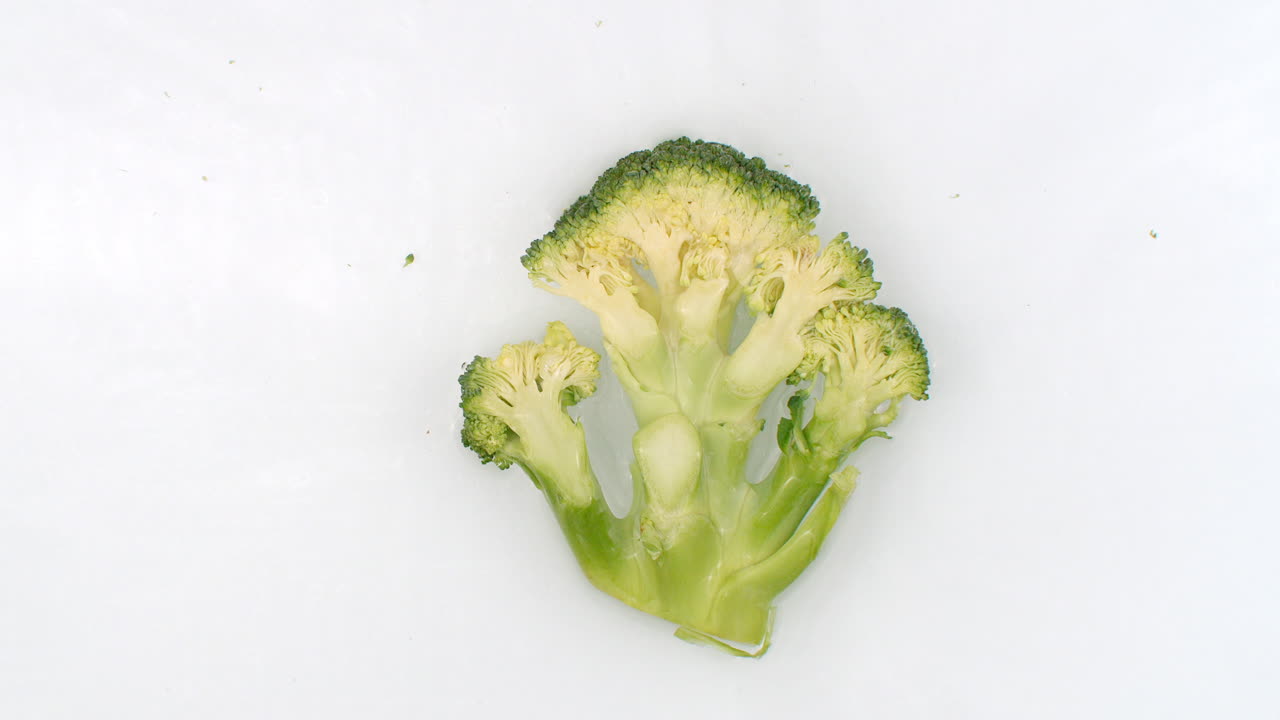 On a white background sliced broccoli is sprinkled with water. Water washes over fresh green broccoli.