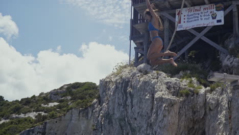 young woman jumps into blue water off of cliffside on greek island, slow motion