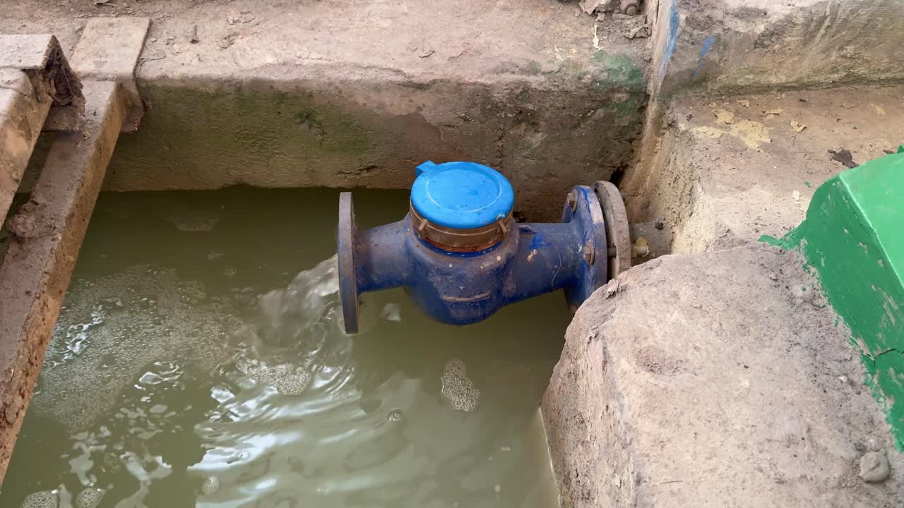 Water flowing out from a large blue industrial pipe with a closed meter cap into wastewater treatment plant