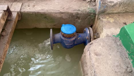 water flowing out from a large blue industrial pipe with a closed meter cap into wastewater treatment plant