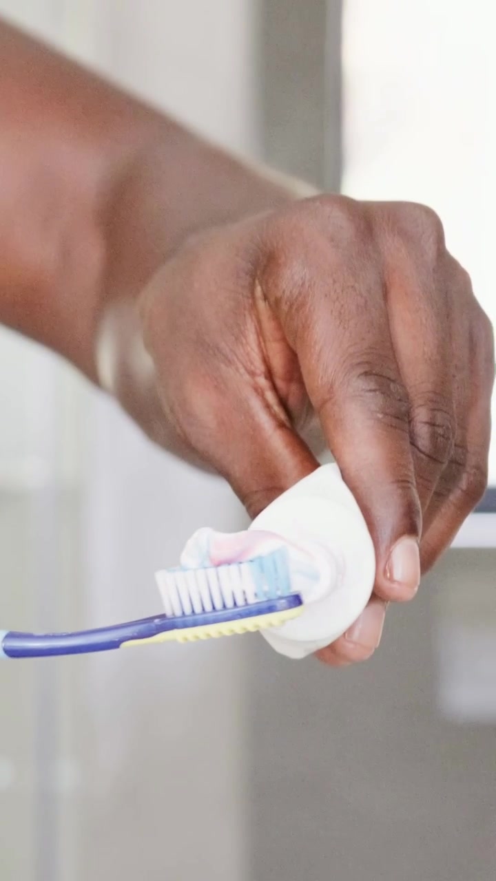 Vertical video: Squeezing tube man's right arm preparing toothbrush at sink wearing white tank top