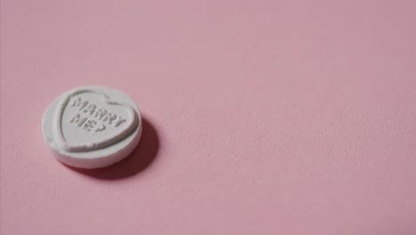 mano recogiendo dulces de corazón con mensaje romántico cásate conmigo en fondo rosa