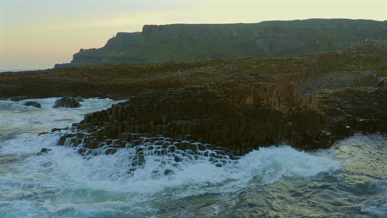 Aerial pullback showcasing the honeycomb rock formations at Giant's Causeway, with crashing waves at sunset