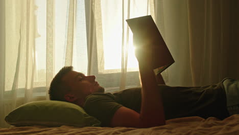 man reading a book in sunlight by the window