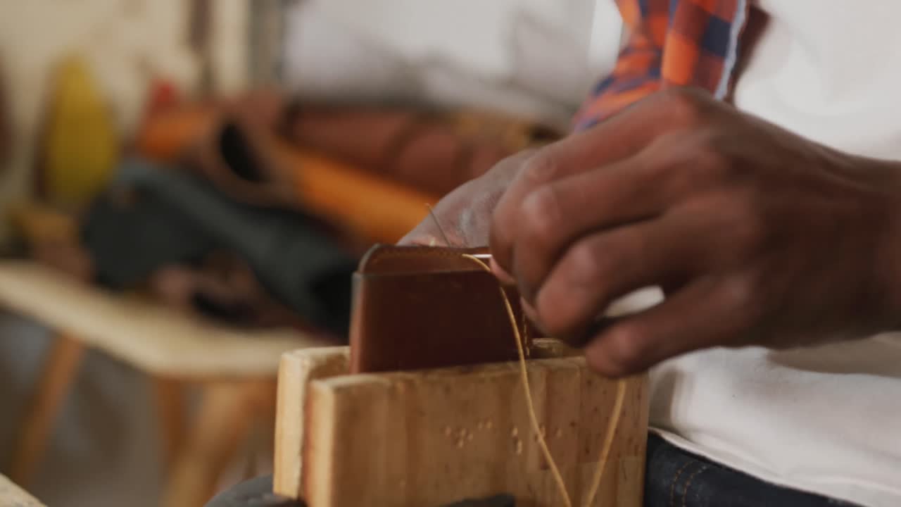 Hands of african american craftsman preparing wallet in leather workshop