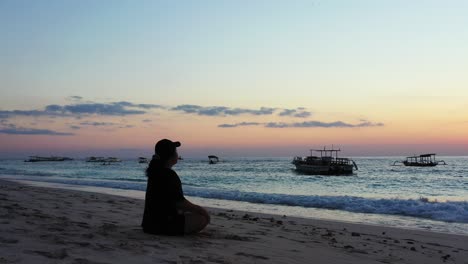 Mujer-Deportiva-Con-Sombrero-Meditando-Temprano-En-La-Mañana-En-La-Tranquila-Playa-De-Arena