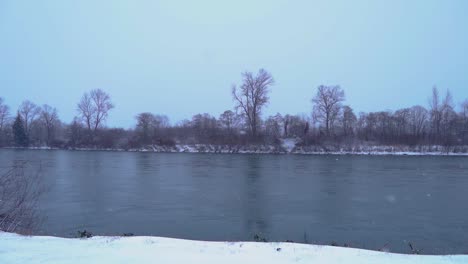 snow falling in storm by river, slow motion, pan to right