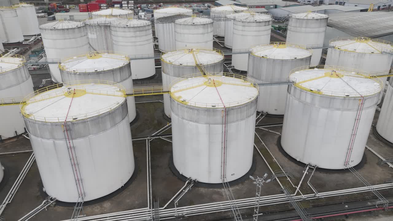 Top-down view of dense riverfront fuel-tank cluster with yellow railings, walkways and pipes illustrating high-capacity petrochemical storage infrastructure