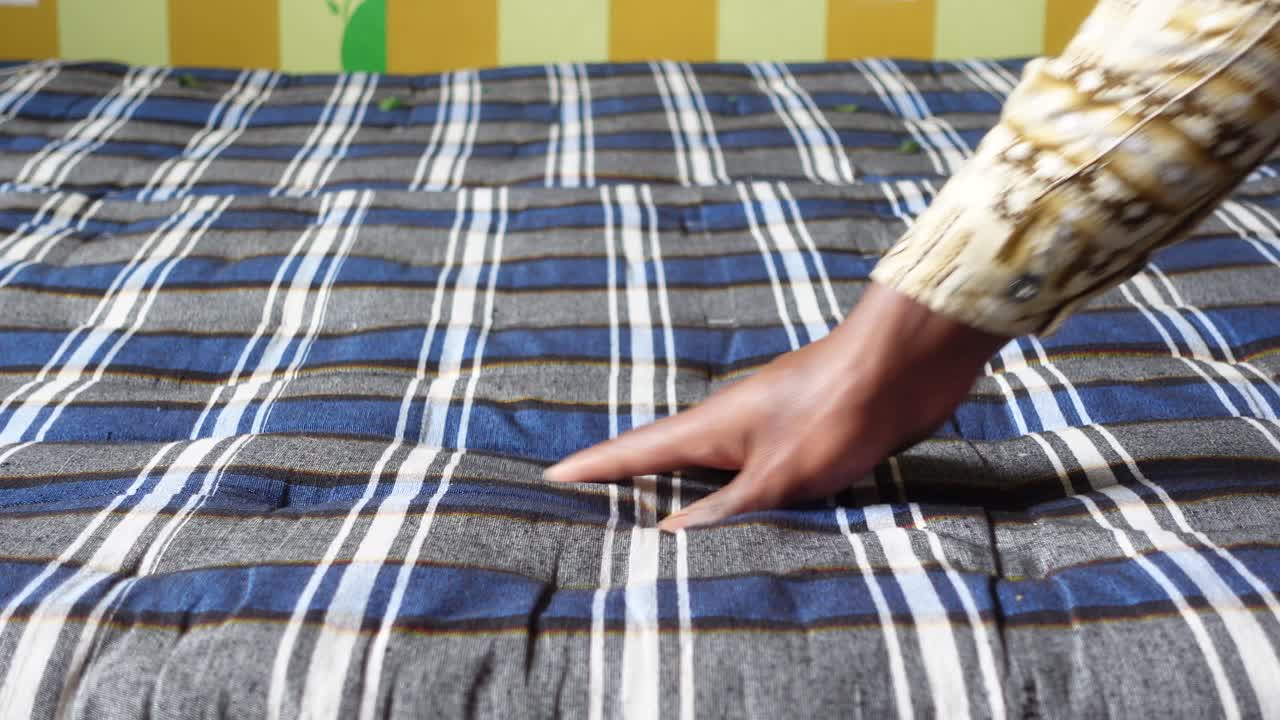 A person's hand pressing on a plaid mattress