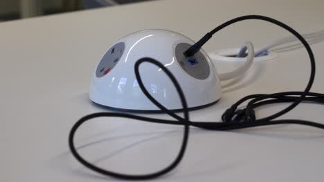 a close up shot of an mixed race man plugging a usb charging cable in to a multi-purpose electrical power point on an office desk