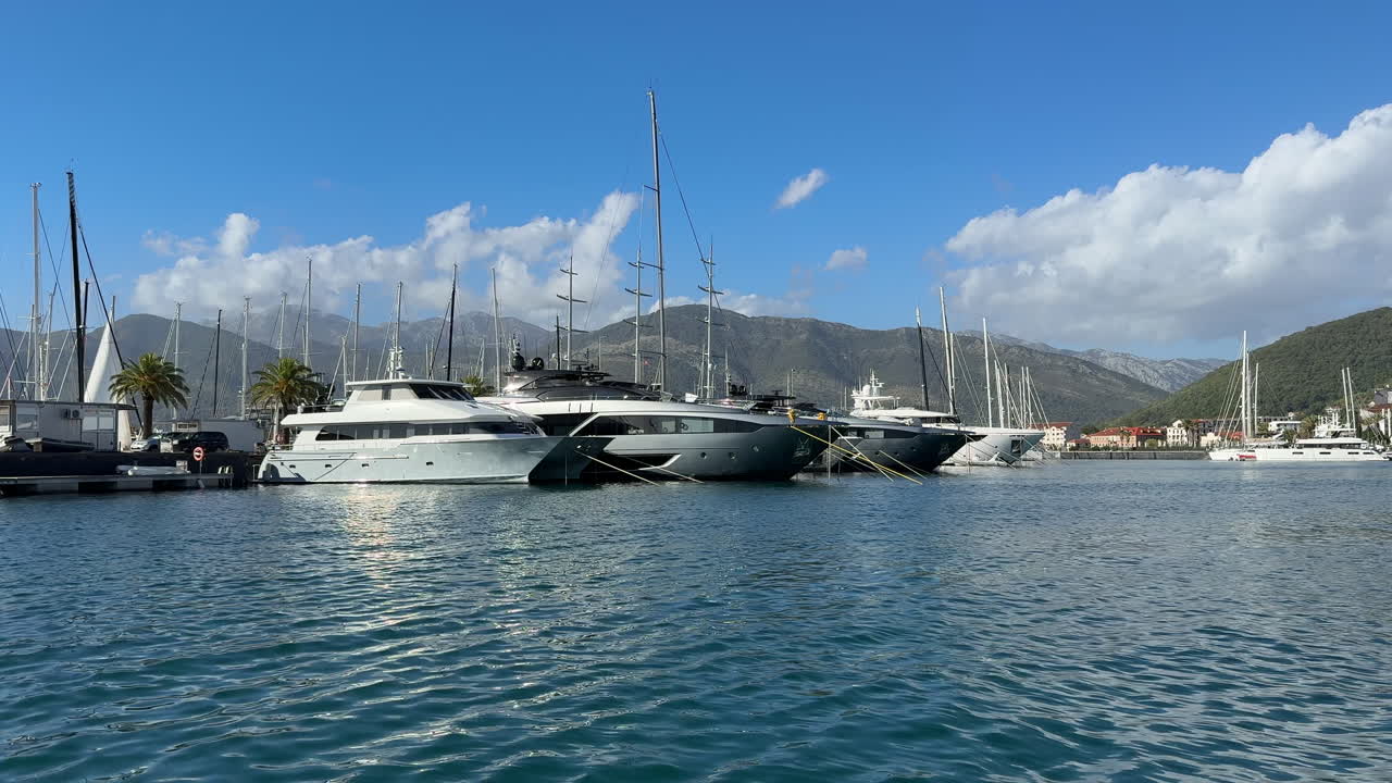 Campo lungo di superyacht di lusso ancorati a Porto Montenegro, con cielo azzurro, acque calme dell'Adriatico e paesaggi montani. Perfetto per immagini di porti turistici, turismo nautico, filmati di viaggi di lusso.