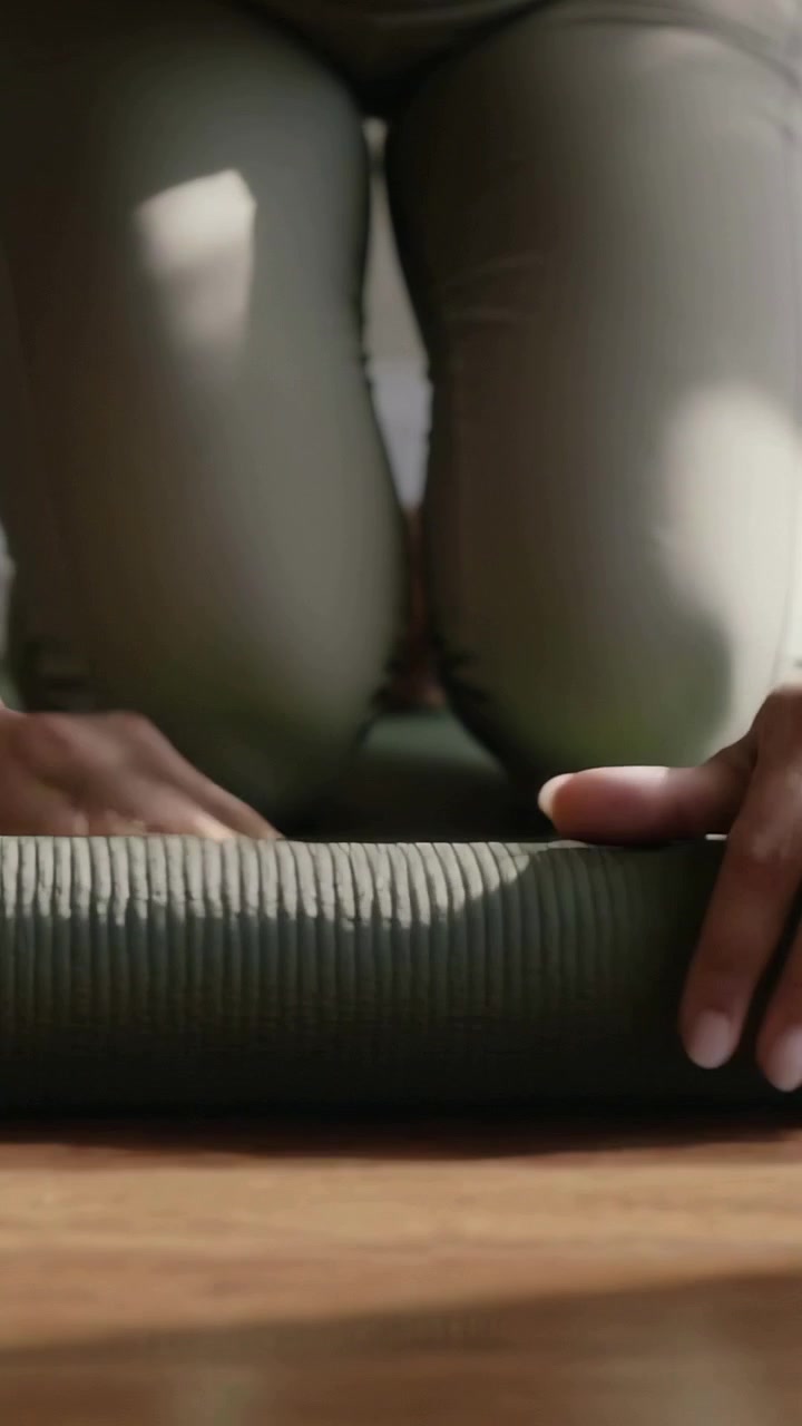 Vertical video: Grabbing kneeling she unrolling dark mat on floor in olive leggings prepping yoga
