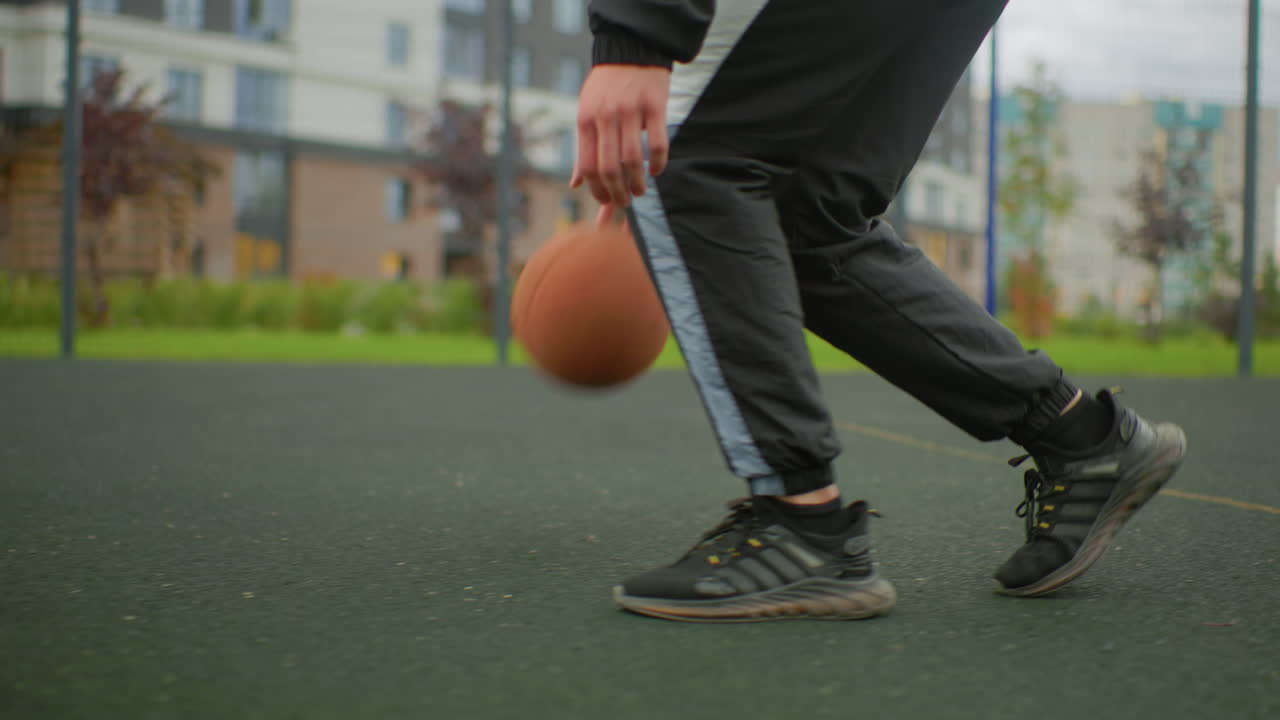 primo piano di un palleggio di pallacanestro sul campo, un atleta si allena con un gioco di gambe preciso e un crossover con scarpe da ginnastica che aderiscono all'asfalto, un movimento ad angolo basso cattura il rimbalzo ritmico, l'energia concentrata e i condomini