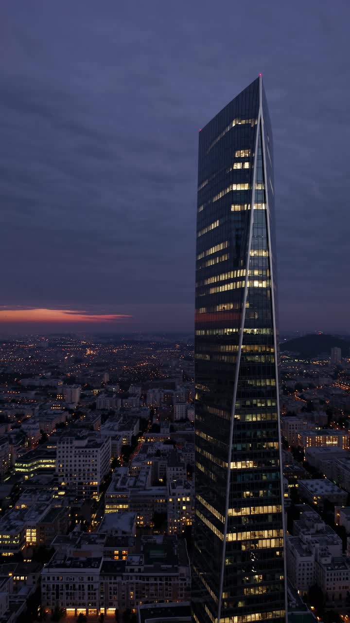 Video aereo ripreso al tramonto che cattura un elegante grattacielo che sovrasta un paesaggio urbano, con luci.