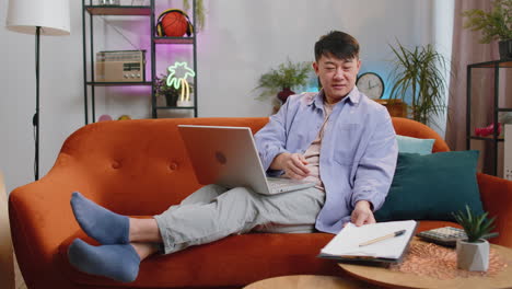 asian business man working with laptop computer and documents planning expenses budget at home