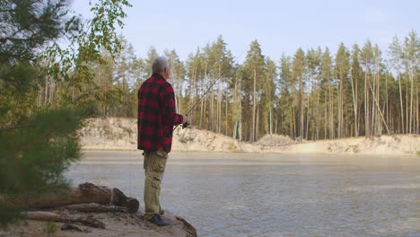 vacation at nature adult man is fishing in freshwater of river resting in forest on shore using rod with reel