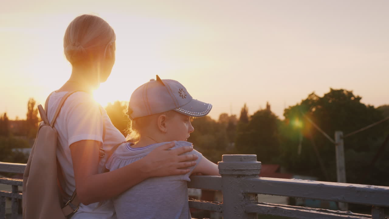 мама и дочь смотрят на город с моста, стоя у перил