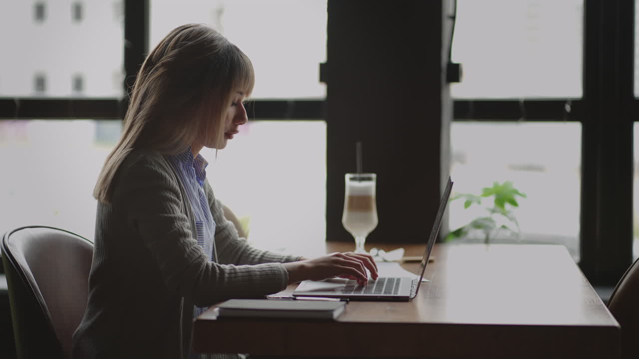 Mixed race woman working from home on laptop computer. Asian lady is using laptop at home typing then taking notes in notebook