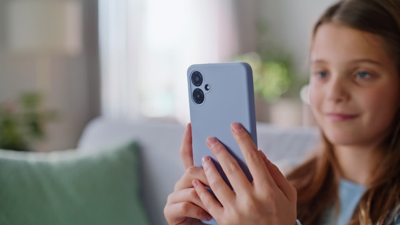 Adolescente felice che guarda lo smartphone e si gode la comunicazione seduto su un divano, primo piano