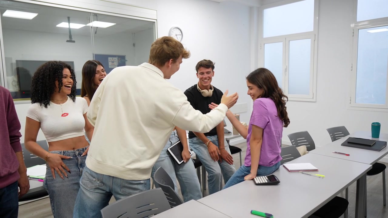 Grupo feliz de estudiantes jóvenes hablando y riendo en el aula.