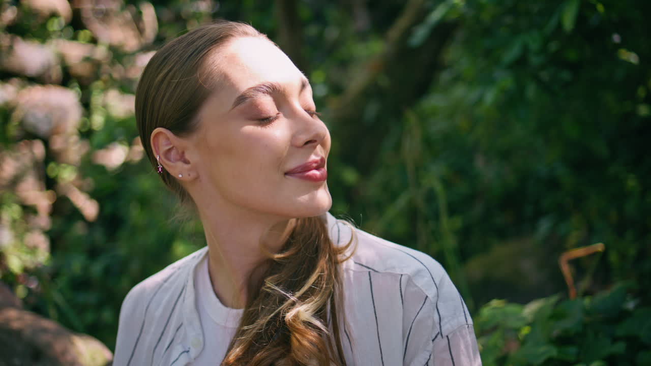 en primer plano, el rostro sereno de una mujer bajo la luz del sol en la vegetación del bosque.