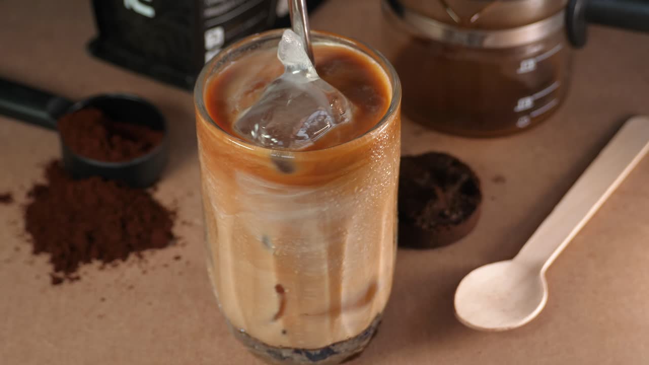Stirring an iced coffee with caramel and ice cubes in a glass, close-up view
