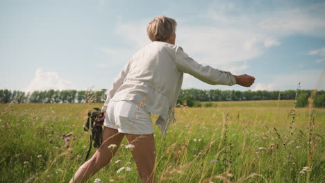 dog trainer throws toy into distance while her dog excitedly runs after it in vast grassy field under clear sky, trainer holds ropes in her left hand, showing playful outdoor interaction