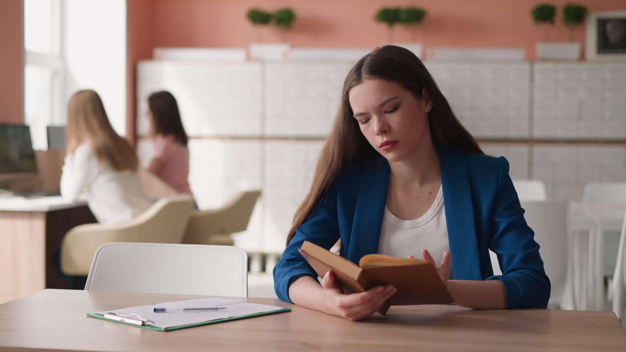 Woman turns page of book sitting at desk in library. Young woman learns literature preparing for exam in college library. Graduate prepares for final test