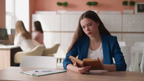 mujer da la vuelta a la página del libro sentada en el escritorio de la biblioteca. mujer joven aprende literatura preparándose para el examen en la biblioteca de la universidad. graduado se prepara para la prueba final