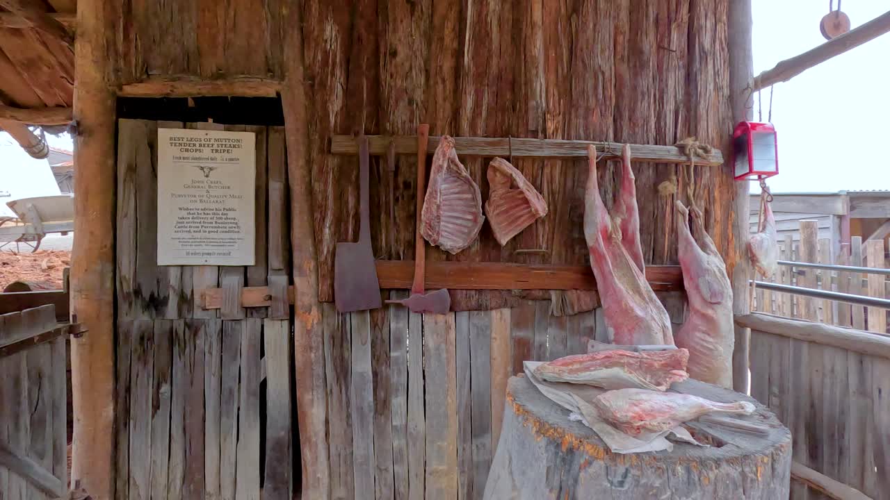 목조 구조물과 함께 역사적인 야외 환경에 설정 된 매달린 고기와 도구와 함께 시골적인 도살점