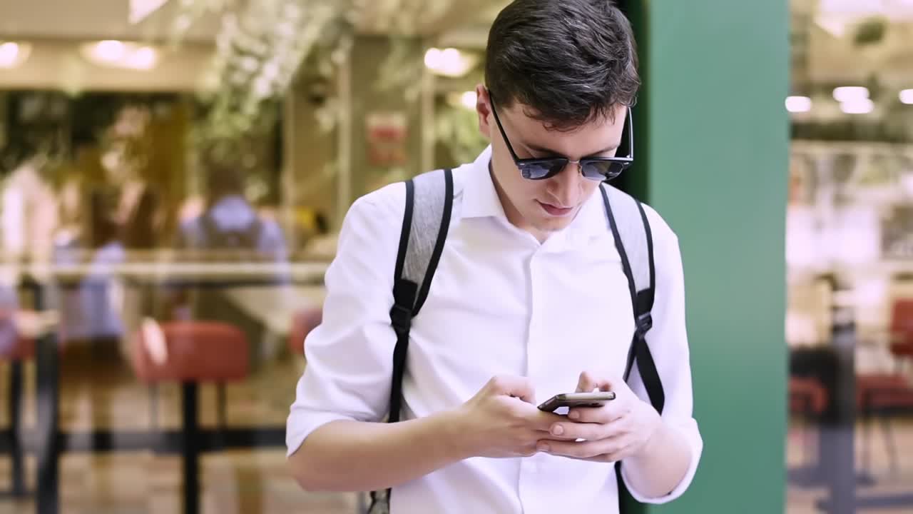 Caucasian man in white shirt and sunglasses writing messages on the phone. Sunny day