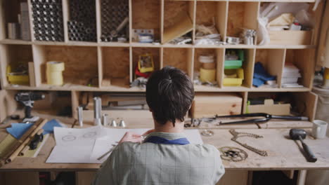 Vista-Trasera-Del-Diseñador-Masculino-En-El-Taller-Trabajando-Hasta-Tarde-En-Componentes-Para-Bicicletas-Construidas-A-Mano.