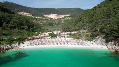 camera slowly moving away from marble beach revealing the white pebble beach with tropical water and lush vegetation, thassos island, greece