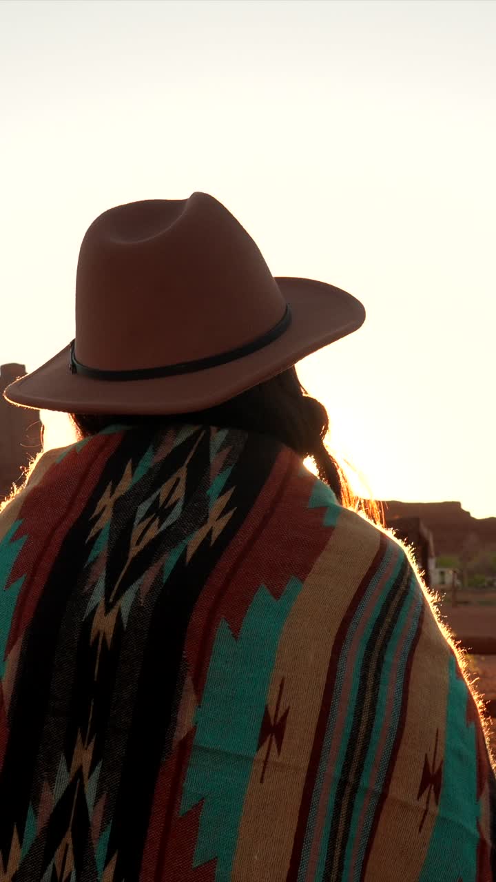 Donna con cappello da cowboy e poncho che guarda il tramonto nel deserto
