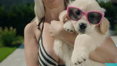 una mujer en bikini sostiene a un cachorro rubio con gafas de sol en sus brazos. verano y vacaciones con un concepto de mascota
