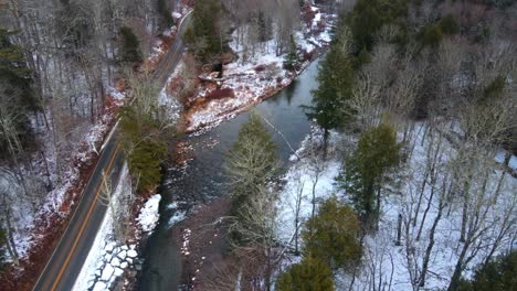 Ariel-view-of-a-snowy-forest-and-stream-running-alongside-a-mountain-in-early-December