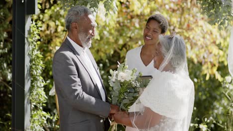 african american woman officiating wedding ceremony of senior biracial couple in garden, slow motion